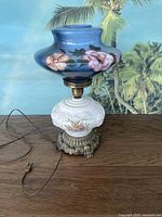 Full view of the vintage globe lamp showing the hand-painted upper globe with pink and orange flowers on blue, white floral embossed glass base, and ornate brass base.