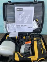 Opened black plastic carrying case showing two Wagner paint sprayers with attached white paint containers and power cords, owner's manuals, and additional accessories.