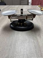Front view of the Weigh Right precision balance scale showing two weighing pans, the calibrated central beam, and four metal counterweights placed on the black base.