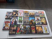 Photo showing 25 assorted used DVD movie cases laid out on floor, variety of genres including action, comedy, drama, sci-fi.