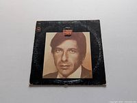 Front cover of Leonard Cohen LP record showing a sepia-toned close-up portrait of Leonard Cohen with a black background. Visible corner wear and edge scuffing.