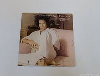 Front cover of Neil Diamond 12 Greatest Hits Vol. II LP showing Neil Diamond seated on a couch in white clothing.