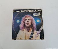 Front cover of the vinyl album 'Frampton Comes Alive!' showing Peter Frampton on stage with guitar and concert lighting.