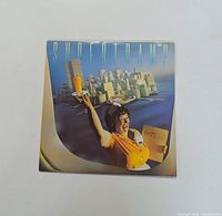 Front cover of Supertramp's Breakfast in America vinyl LP showing waitress with orange juice and cityscape background.