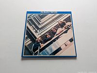 Front cover of The Beatles 1967-1970 vinyl LP showing band members looking down from balcony with blue border.