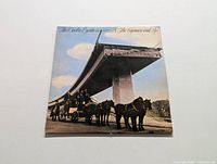 Front cover of The Doobie Brothers 'The Captain and Me' vinyl album showing horse-drawn carriage beneath partially constructed highway.