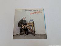 Front cover of The Monks 'Bad Habits' vinyl LP showing a seated figure dressed as a nun, sitting on a wooden stool next to a table.