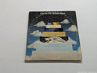 Front of the album cover showing the stacked design of album titles on a blue sky with clouds background.