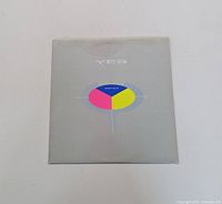 Front of Yes 90125 album sleeve showing band name and colorful circular design on gray background.