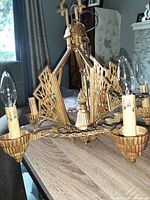 Front angle of gold-toned 5-arm metal chandelier showing decorative fan panels and candle-like light sockets