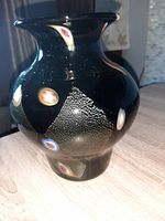 Single black art glass vase displayed on wooden surface, showing front triangular gold texture and colorful eye-shaped round elements.