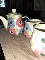 Three-piece porcelain tea set with teapot and two cups, floral design in red, blue, green on white base.