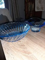 Side view of two blue depression glass bowls on wooden table, showing ribbed swirl pattern on larger bowl and flower frog base on smaller bowl.