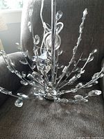 Close-up of the base and one side of the chandelier showing chrome branches with clear crystal-like droplets attached.