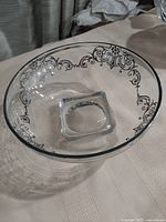 Clear crystal bowl with embossed silver decorative rim and raised square base shown from an overhead angle, highlighting the full ornate rim design and transparency of the bowl.