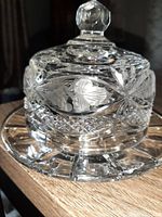 Close-up of crystal butter dish lid with cut glass leaf and grape design and faceted knob on top.