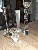 Four assorted vintage candlesticks shown on wooden table, including tall metal and glass types.
