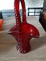 Full view of red glass basket showing twisted handle and scalloped rim.