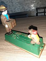 Side angle showing the man holding a box on the green base with the monkey figure on the lever.