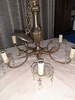 Front view of vintage 6-arm brass chandelier showing arms, candle-style sockets with fabric-like covers, glass bobeches with hanging crystals, and central column.