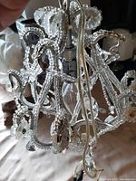 Close-up photo showing intricate crystal bead work and flower-shaped crystal accents on the vintage chandelier, along with visible aging and old wiring.