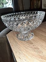 Clear molded crystal fruit bowl on wooden surface, showing textured pattern and pedestal base.