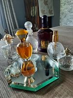 All six assorted vintage perfume bottles displayed on a hexagonal mirrored tray on a wooden surface with background showing home interior.