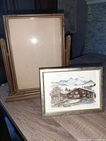 Photo showing large vintage swinging gold-tone Art Deco picture frame alongside smaller framed mountain cabin art