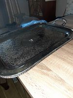 Angled close-up showing ornate engraved floral and scroll designs on the silver plate tray with visible beaded edges