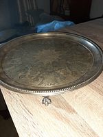 Full view of round silver plate serving tray with beaded edge and clawfoot feet, displaying tarnish and patina.