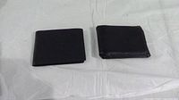 Two black leather wallets side by side on white fabric background showing one with visible wear and the other appearing unused.