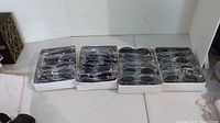 Four boxes of sunglasses arranged in rows on a white surface, each box containing 12 pairs.