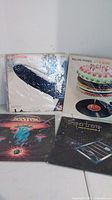 Photo showing four vinyl album covers: Led Zeppelin with significant cover wear, The Rolling Stones 'Let It Bleed' with cake cover art, Boston album with spaceship illustration, and Supertramp 'Crime of the Century' with man behind bars.