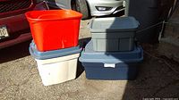 Stacked gray, white, and red plastic storage bins showing attached lids on gray and white bins and no lid on the red bin.