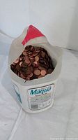 Plastic Maqua 5 litre jug partially open showing 3/4 full of mixed US and Canadian pennies inside.