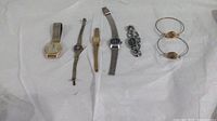 Overview of all seven watches lying on white cloth, showing various metal bands and styles.