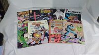 Photo of 9 comic books spread out showing colorful action-themed covers and titles.