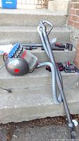 Dyson Big Ball Extra vacuum canister with attached hose, primary handle, and various attachments laid out on concrete steps.