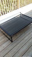Full view of the Veehoo elevated dog bed with black mesh fabric on a wooden deck.