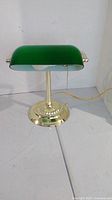 Desk lamp showing front and base with green glass shade, gold-tone finish, pull chain switch.