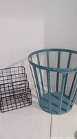 Photo of blue metal basket and black wire metal organizer side by side on white surface with plain wall background