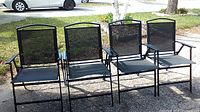 Set of 4 outdoor black metal chairs with mesh seats and backs arranged in a row.