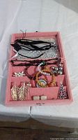Pink small jewelry case containing assorted costume jewellery including earrings, multiple bracelets, and necklaces displayed inside compartments.
