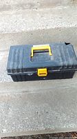 Closed black plastic toolbox with yellow handle and latch, visible hole on side