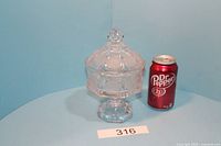 Clear full view of the antique Fostoria coin glass candy covered dish with lid, next to a soda can for scale.