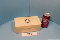 Closed view of ivory colored Art Deco style jewelry box with black and white cameo medallion on top, measuring approximately 8 x 4.5 x 3 inches and positioned next to a soda can for scale.