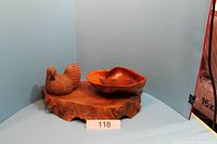 Photo showing wooden chicken figurine, wooden bowl, and natural wood base from a side angle.