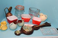 Full lot showing all items: Fire King glass measuring cup, Pyrex red and white square dishes, small ceramic jugs, copper pourer, glass jar with seal, wooden barometer and thermometer, and rectangular glass dish.