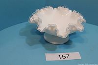 Front view of milk glass bowl showing ruffled edges and clear rim trim on blue background.