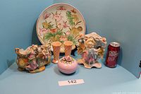 Photo of the entire set showing a decorative plate at the back with butterflies and pink flowers, two figurine planters on either side, two pink vases in front of the plate, and a pink covered container in front center. A Dr Pepper can is placed for size reference.